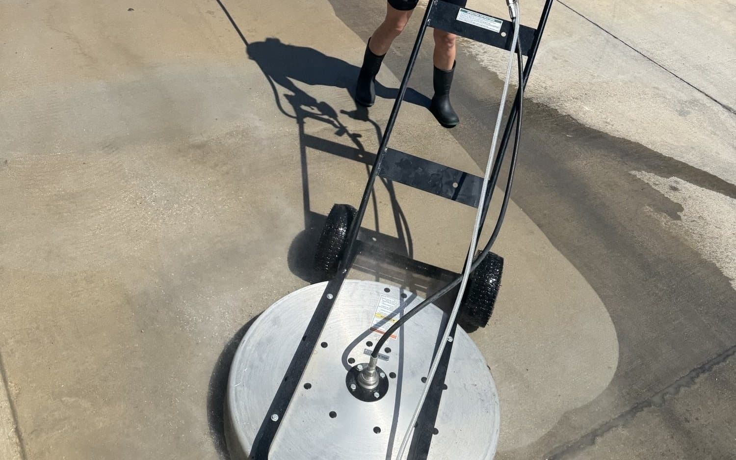 Brooke Wakeland of Ascension Exterior Services running a surface cleaner across a driveway, the cleaned concrete visibly lighter